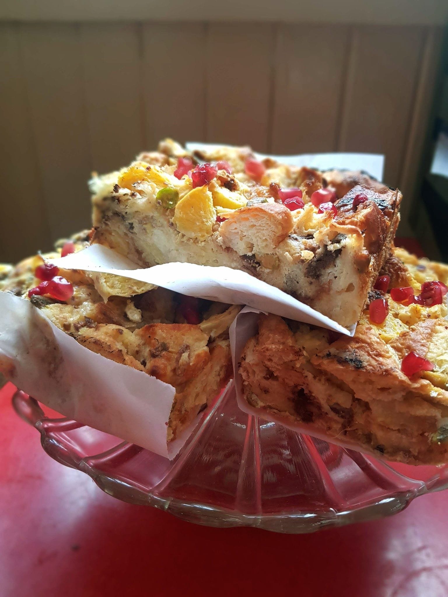 A glass cake stand loaded with large slices of bread and butter pudding