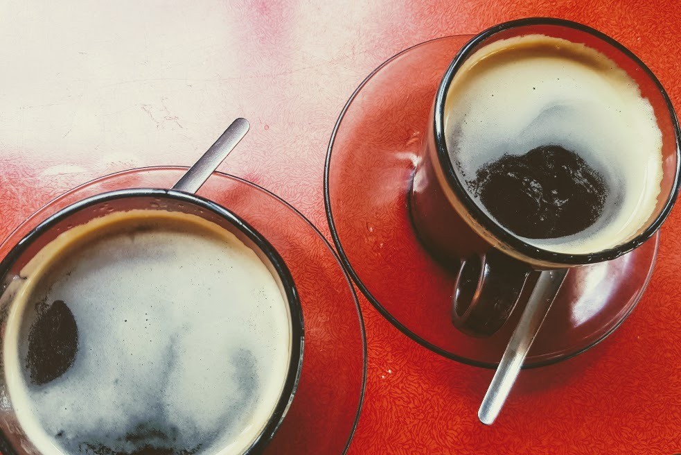 Two cups of black coffee americano in vintage brown glass cups and saucers on deep red table